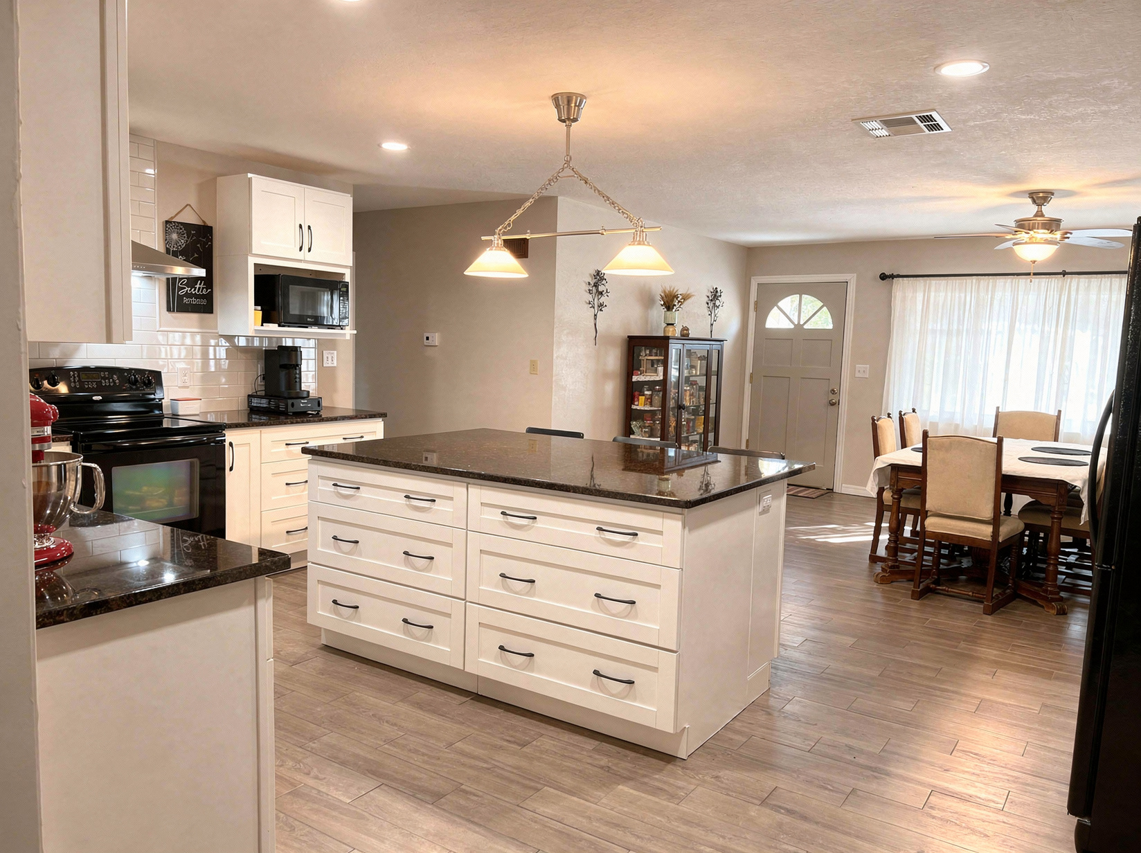 A bright kitchen with white cabinets, a dark stone island, and an adjoining dining area.