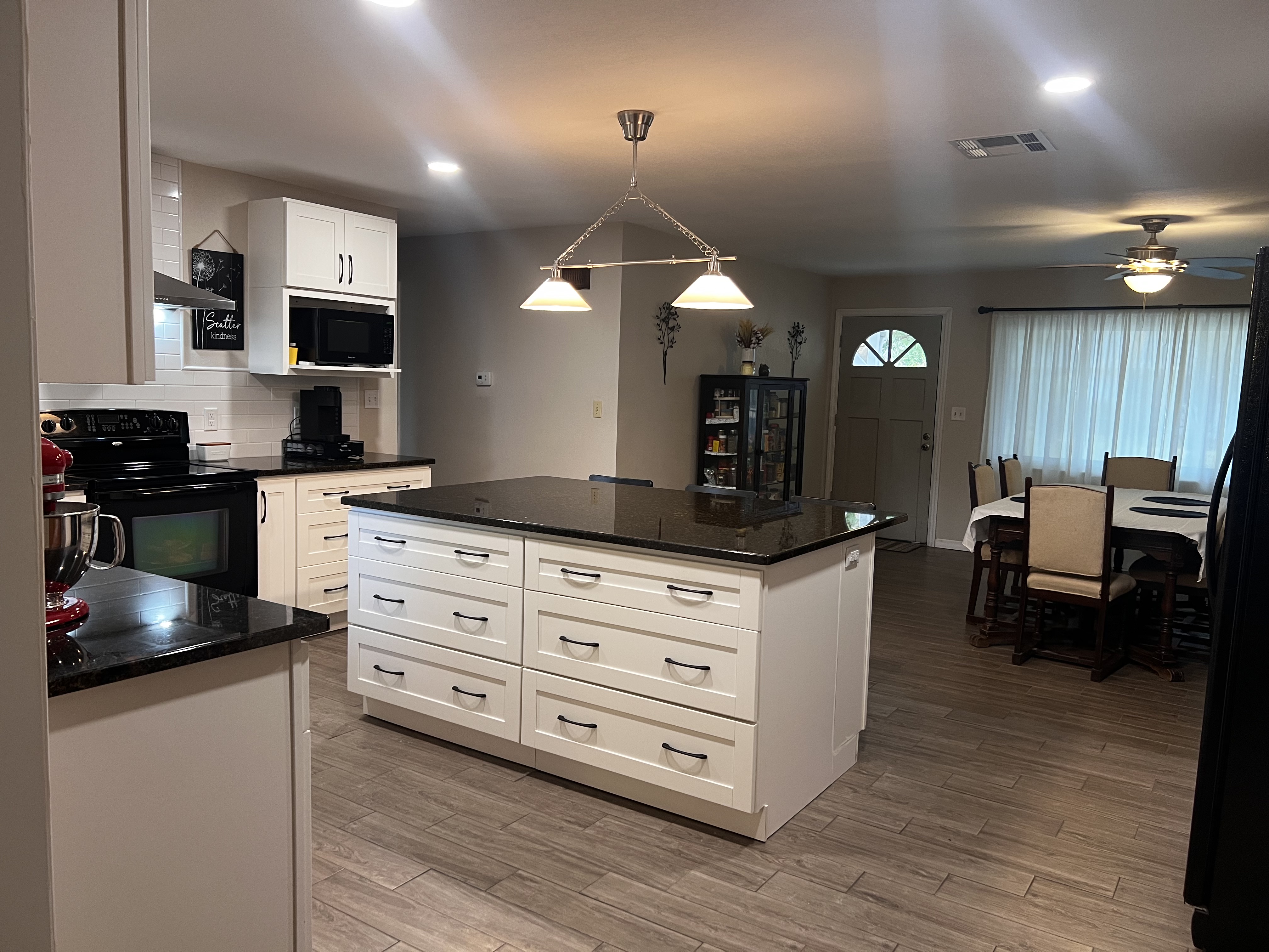Original kitchen photograph: mixed light, bright ceiling fixtures, and shadows across the island and dining area.